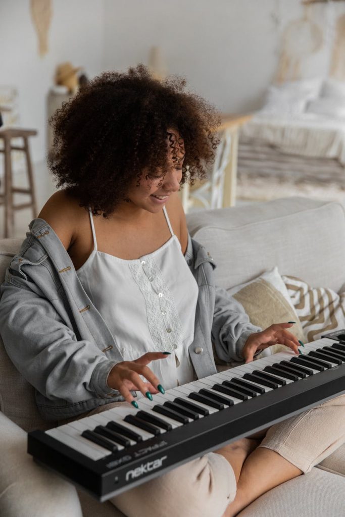 happy ethnic woman playing synthesizer sitting on couch at home